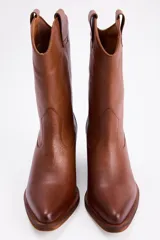 Bota estilo western de caña media, confeccionada en gamuza color marrón con bordados decorativos en hilo claro. Cuenta con taco cuadrado de madera y tiradores laterales.