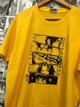 Remera amarilla con estampado de personajes de Naruto en recuadros negros con texto en japonés. El estampado incluye a Naruto, Sasuke, Sakura y Kakashi.