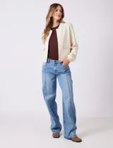 Camperita tipo bomber color beige claro, con cuello redondo acanalado, cierre frontal con broches metálicos y bolsillos delanteros con tapa. Los puños y el bajo son acanalados.