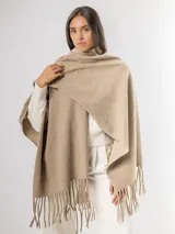 Ruana de tejido suave en color beige, con diseño envolvente y terminaciones con flecos en el ruedo.
