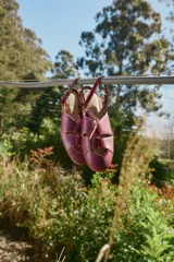 Sandalias planas tipo slingback de cuero bordó, con diseño delantero calado, silueta de punta redonda y tira trasera ajustable con hebilla.