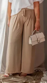 Cartera de mano color beige con solapa frontal y cierre metálico en forma de D. Incluye asa superior y correa ajustable.