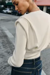 Jersey de punto de cuello redondo y manga larga, con diseño estructurado que incorpora hombreras marcadas y detalles de pliegues en los hombros.