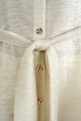 Camisa larga fluida de color crema con cierre frontal de botones, mangas tres cuartos anchas y cinturón ajustable para anudar en la cintura.