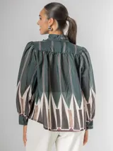 Camisa de manga larga con cuello alto y lazo para atar, confeccionada en tela liviana con estampado geométrico en tonos verde oscuro, blanco, beige y marrón.