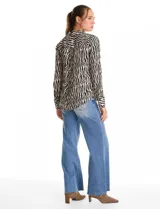 Camisa de manga larga con cuello solapa y cierre frontal de botones. Presenta un estampado de cebra en tonos blanco y negro, con puños abotonados y ruedo redondeado.