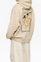 Sudadera larga de corte recto color beige, con escote redondo y capucha ajustable. Presenta mangas largas con forma, logo estampado en el pecho y cordones personalizados con nudos.