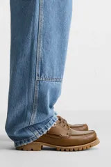 Zapato tipo náutico de cuero color marrón, con cordones, ojales metálicos laterales y suela de goma con volumen y relieve dentado.