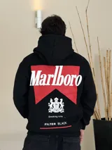 Canguro negro con capucha, de corte boxy, con estampa gráfica en la espalda que recrea el logo de Marlboro en rojo y blanco, junto con el escudo de Philip Morris y la leyenda 'Smoking kills' y 'FILTER BLACK'.