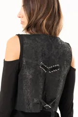 Chaleco de cuero con acabado desgastado, estilo western, con cierre frontal de botones metálicos y detalles de ojalillos con entrelazado de cuero en la parte superior delantera.