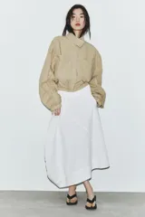 Falda midi blanca de tiro medio con bolsillos delanteros y bajo asimétrico. Cierre lateral con cremallera oculta.