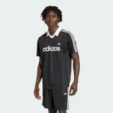 Camiseta Adidas Originals de manga corta, color negro con sutiles rayas verticales, cuello polo en V de color blanco, al igual que las líneas características de la marca en los hombros. Cuenta con el logotipo de la marca y la inscripción "adidas" en el pecho en color blanco.