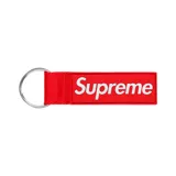 Llavero de cinta textil roja con etiqueta de goma rectangular que presenta el logo de Supreme en color blanco y argolla metálica.