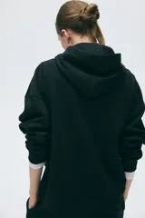 Buzo canguro negro con interior cepillado suave, capucha de doble capa, hombros caídos y bolsillo frontal.