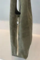 Bolso tipo tote de gran capacidad, confeccionado artesanalmente en cuero vacuno color marrón. Presenta un diseño minimalista con costura central vertical, fuelle lateral ajustable con cierre y placa metálica con logo en la parte inferior.