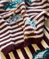 Sweater artesanal de punto tejido a mano en 100% lana merino, con diseño de rayas horizontales en color bordó y crudo, y detalle de diseño floral bordado en la parte frontal.