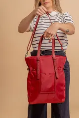 Bolso tipo tote bag de símil cuero color rosa pálido, con asas dobles y detalles de costura en color beige claro. Presenta un bolsillo frontal rectangular aplicado y herrajes metálicos.