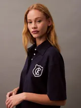 Chomba azul marino de punto de algodón con cuello clásico, tapeta con botones ocultos y mangas cortas. Presenta un corte holgado y un escudo bordado con el logo de Calvin Klein en el pecho.