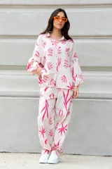 Conjunto de dos piezas compuesto por camisa de corte oversize con mangas largas y pantalón de corte recto, ambos confeccionados en tela color crudo con estampado botánico en color verde.