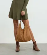 Cartera tipo hobo de gran tamaño confeccionada en material sintético efecto gamuza color tostado. Presenta una estructura flexible, asa única en tono contrastante y cierre mediante botón a presión.
