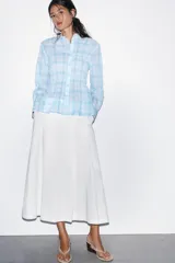Falda midi de tiro alto en color blanco, con diseño acampanado y detalle de pliegues frontales. Cuenta con cierre lateral mediante cremallera oculta.