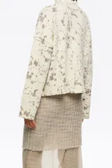 Jersey corto de corte boxy confeccionado en mezcla de lana, con cuello alto y mangas largas rectas, de color beige con diseño estampado tipo efecto salpicado en tonos gris y marrón.