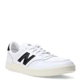 Championes New Balance modelo Court, color blanco con logo "N" y detalle en el talón en negro. Diseño de caña baja con cordones blancos y suela color crema.