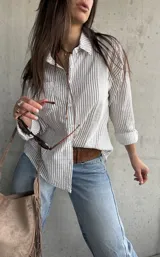 Camisa de corte oversize, con diseño a rayas verticales marrón sobre fondo blanco, manga larga, cuello camisero y bolsillos frontales.