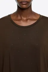 Vestido largo de corte holgado en color marrón, con cuello redondo y mangas largas de tul superpuestas. Presenta un diseño minimalista con sutiles detalles brillantes en el tejido principal.