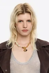 Collar de diseño mixto que combina una sección de perlas irregulares con una sección de cadena de eslabones dorados. Incluye un cierre tipo barra en T y dos dijes colgantes en forma de corazón, uno dorado con logo grabado y otro esmaltado en negro.