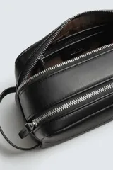 Neceser negro con textura grabada, cierre de doble cremallera y asa lateral. Interior con bolsillo con cremallera. Marca Mango.