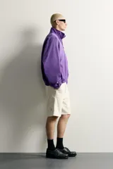 Cazadora relaxed fit de denim de algodón en color violeta, con efecto lavado, cuello alto, cierre frontal de cremallera y bolsillos en las costuras laterales. Presenta puños y dobladillo elásticos.