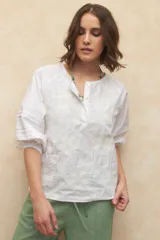 Blusa blanca de algodón con bordado floral, cuello mao, mangas 3/4 abullonadas con elástico en los puños y cierre frontal parcial con botones.