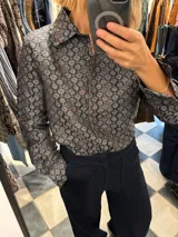 Camisa de manga larga con estampado de flores pequeñas en tonos blanco, naranja y celeste sobre fondo negro.