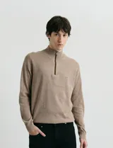 Sweater de punto color verde oliva, con cuello alto y medio cierre frontal. Presenta coderas en símil nappa y puños acanalados.