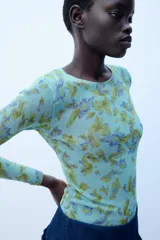 Jersey de punto Zara con cuello redondo y manga larga, con estampado floral a contraste en tonos verdes y morados sobre base celeste.