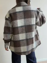 Sobrecamisa de paño con diseño a cuadros en tonos marrones, grises y blancos. Presenta cuello clásico, cierre frontal con botones y bolsillos delanteros con tapa.