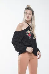 Blusa negra con mangas largas abullonadas, hombros descubiertos, cuello halter cruzado y bordado floral en el pecho.