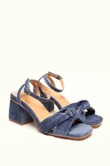 Sandalia de tacón cuadrado medio, confeccionada en terciopelo color azul. Presenta un diseño de tiras cruzadas con nudo en la parte frontal y cierre de pulsera con hebilla ajustable al tobillo.