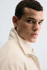 Cazadora de tejido color crema, con cuello alto, cierre frontal de cremallera y bolsillos de vivo en la cadera. Presenta un calce relajado (relaxed fit).