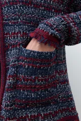 Chaqueta de tejido de punto con textura, diseño multicolor en tonos azul, rojo y blanco. Presenta cuello redondo, cierre frontal y detalles de flecos en los bordes y puños.