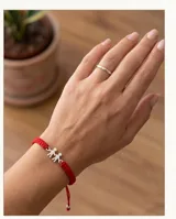 Pulsera de hilo rojo tejida en macramé con dije central de dos figuras de niños en plata 925 y terminaciones con esferas de plata. Diseño ajustable.