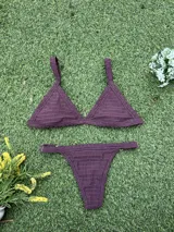 Conjunto de bikini color bordó de tejido fruncido, compuesto por un corpiño de triángulo fijo con tirantes anchos y una bombacha colaless regulable con argollas doradas en los laterales.