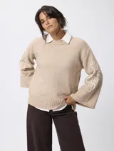 Sweater de tejido de punto color beige, con cuello redondo, mangas largas acampanadas y diseño bordado en color blanco en las mangas.