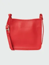 Cartera bandolera Longchamp modelo Le Foulonné S, color rojo vibrante, de cuero granulado. Presenta un diseño cuadrado con correa ajustable y hebilla metálica dorada. El logo de la marca está grabado sutilmente en el centro.
