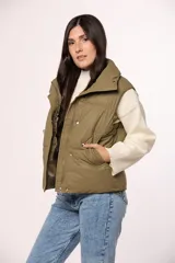 Chaleco puffer de nylon en color verde oliva, con cuello alto, cierre frontal con cremallera y botones a presión, y bolsillos laterales.