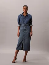 Falda midi de denim azul de talle alto, con diseño carpenter, cierre frontal de botón y cremallera, bolsillos y abertura central delantera.