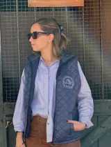 Chaleco acolchado azul marino con diseño pespunteado en rombos, cuello alto y cierre frontal con cremallera. Presenta un bordado institucional en el pecho y bolsillos laterales.