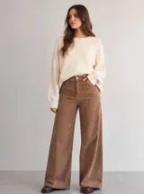 Pantalón de pana color tostado con corte wide leg y tiro alto. Presenta diseño clásico de cinco bolsillos, cierre frontal con botón y una caída recta y amplia.