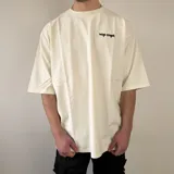 Remera oversize color beige, con cuello redondo, mangas cortas y pequeño estampado en el pecho con el texto "vcp cnpt.".